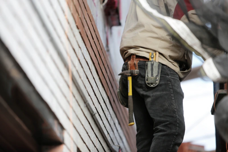 Monthly Maintenance Tasks A man on a ladder wearing a tool belt, engaged in home maintenance tasks.