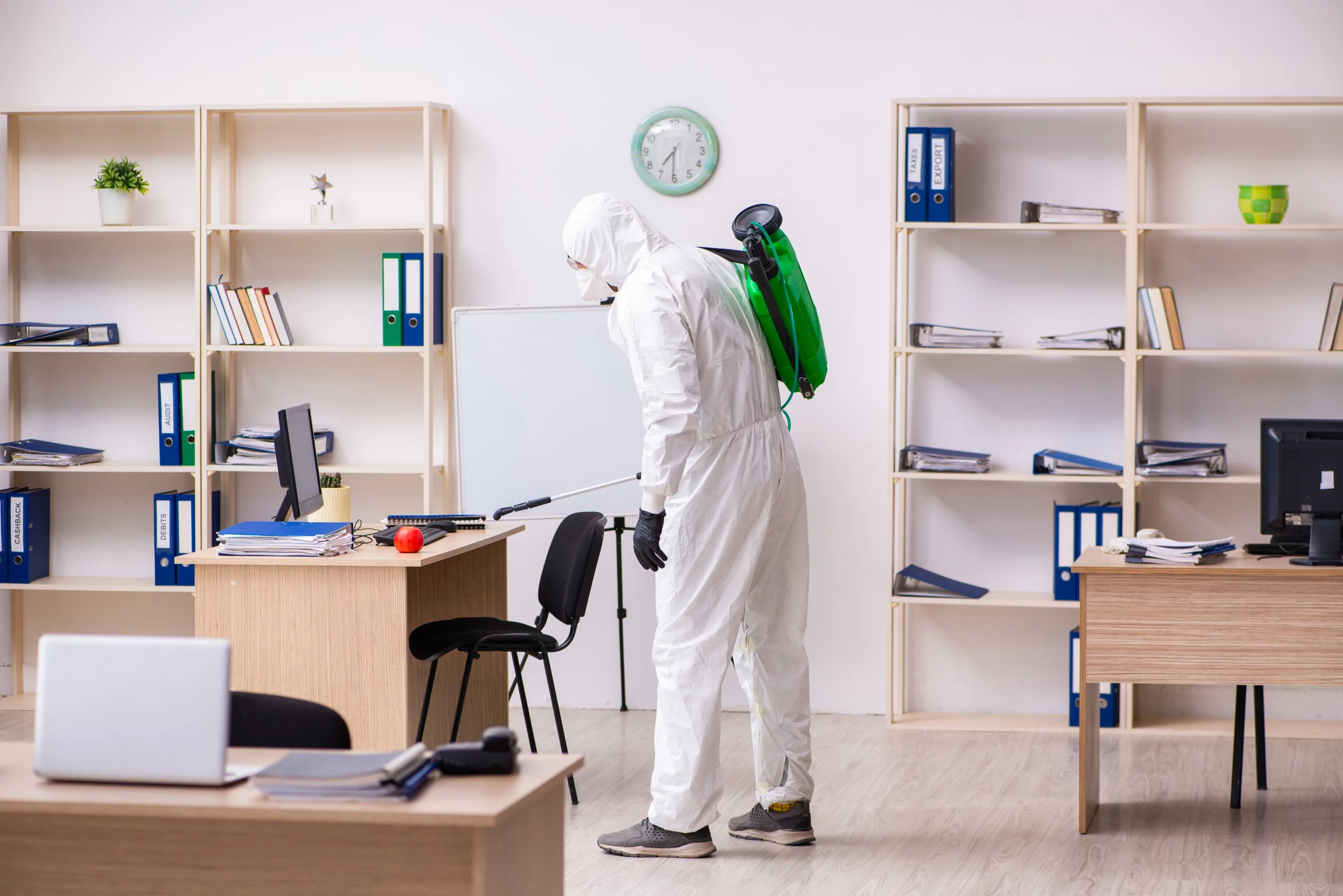 Office Pests A Guide to Workplace Pest Prevention A man in a white suit and green backpack cleans a room, implementing pest control measures to prevent infestations for workplace pest prevention.