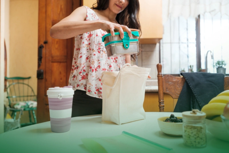 Go Green_ Simple Steps for a Greener Home Start the Year Right: Your Easy Guide to a New Year 2024_A woman taking lunch in reusable containers and putting them in a bag made of fabric for a sustainable lifestyle.